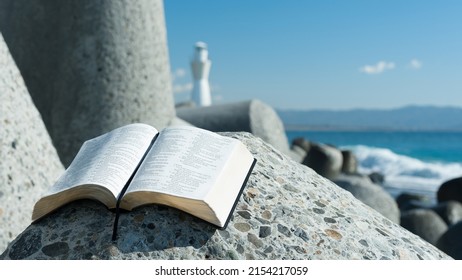 Tagonoura Port, Fuji-Shi, Shizuoka-Ken, Japan - January 21, 2019: Holy Bible open to Psalm 119 on top of a breakwater. Beautiful blurred background with white lighthouse and sea with waves.