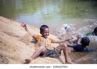 Taherpur, Bangladesh – November 05, 2019: Selective Focus On The Child Toppling From The Sands Of The Riverbank Down To The Water. Little Kids Enjoying Tumbling With The Sands And Bathing In A River.