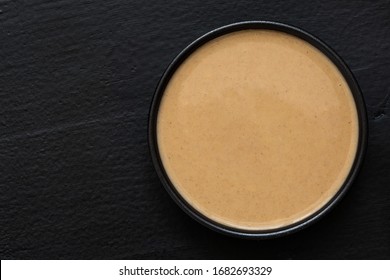 Tahini In A Black Ceramic Bowl Isolated On Black. Top View. Copy Space.