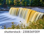 Tahquamenon Falls with thistle weeds growing beside river and basin with cliff walls on other side