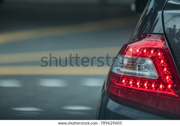 A tail light of the grey car on\
the street background. Red back light for car when stopping.\
