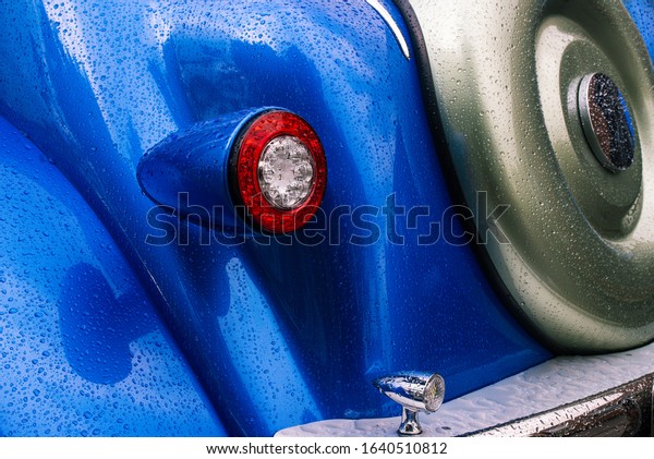 Tail light and spare tire of a retro car. Detail of\
the interior of a vintage car. Chrome bumper and spare wheel.\
Classic car in blue.