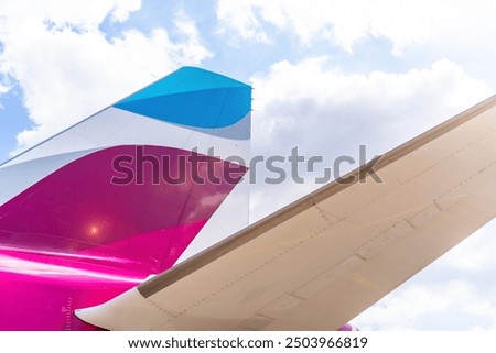The tail of a plane is shown in a close up. The tail is pink and blue
