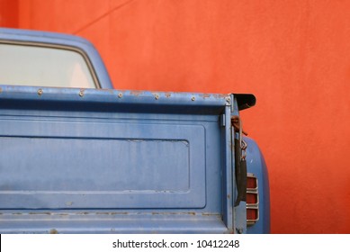 The Tailgate Of A Blue Battered Sixties American Pickup Truck In Front Of A Red Wall