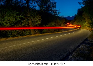 Taillights Illuminate An Empty Road In A Summer Night Forest. Long Winding Trails