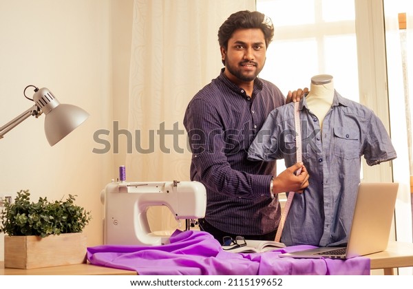 tailor asian man designer sewing clothes\
on sewing machine next to laptop studio\
workplace