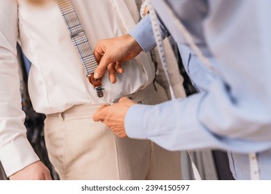 Tailor attaching suspenders to client's trousers in a suit fitting session at a wedding store - Powered by Shutterstock