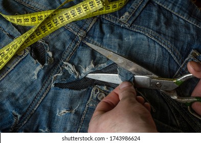 A Tailor Cuts A Piece Of Denim From Old Ripped Jeans. Men's Hands Work With Metal Vintage Scissors. Craft Tailor. View From Above.