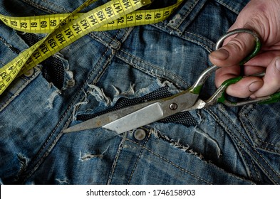 A tailor cuts a piece of denim from old ripped jeans. Men's hands work with metal vintage scissors. Craft tailor. View from above.