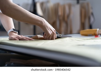 Tailor hand hold scissors cut fabric material for sewing. Closeup of work process of clothes creation in workshop studio or professional atelier. Garment industry and dressmaking occupation concept - Powered by Shutterstock