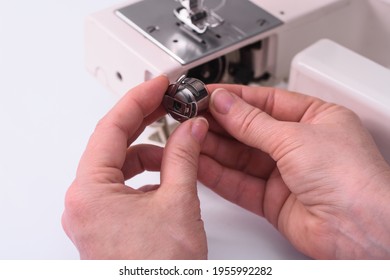 The Tailor Holds A Metal Bobbin With Thread In His Hands Before Inserting It Into The Sewing Machine.