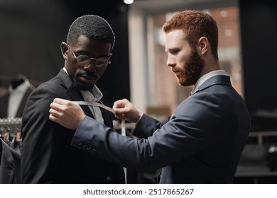 Tailor measuring client for bespoke suit. Young man African American businessman in tailoring studio. - Powered by Shutterstock