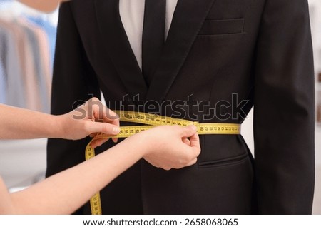 Tailor measuring jacket on man in atelier, closeup