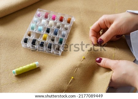 Tailor with needle in hands sews clothing. Woman seamstress at workplace. Closeup needlework