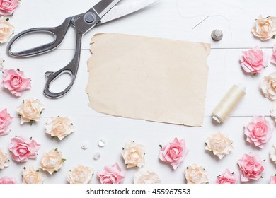 Tailor scissors with sewing tools and old paper sheet with copyspace on white wooden background