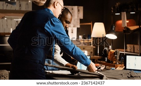 Tailor and trainee cutting garment in workshop, using cut fabric to create modern clothing items. Experienced couturier teaching apprentice to handcraft clothes in tailoring atelier.