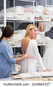 Tailor Tying Pink Satin Belt Around Waist Of Happy Bride During Wedding Gown Fitting In Dressmaking Studio