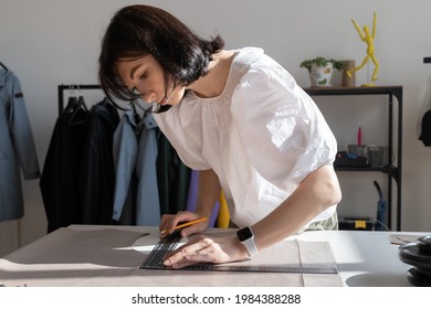 Tailoring Process: Girl Dressmaker Measuring Cloth Material For Sewing Clothes. Young Female Tailor Use Ruler To Cut Fabric And Draw Pattern. Creative Fashion Design Workshop Studio With Sewer Working