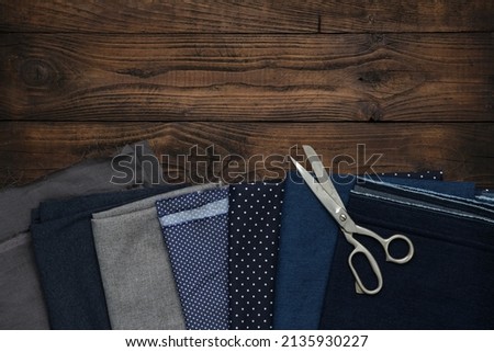 Tailoring scissors and set of fabrics for sewing on wooden board. Top view, flat lay.