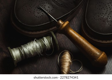 Tailoring and shoe repair. Shoes and an awl with threads on a wooden table