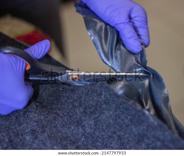 Tailor\'s hands in blue, rubber gloves while\
working with fabric.Tightening of the car interior.The hands of a\
girl in blue gloves while working with scissors with fabric\
selective focus.