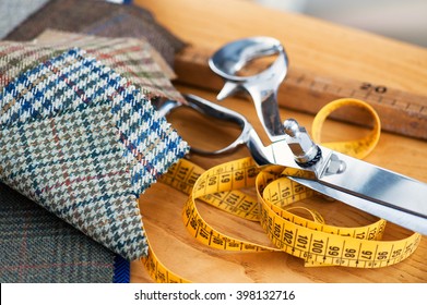 Tailors tools on a wooden workbench with assorted patterned fabric swatches, a tape measure, a large pair of scissors and a wooden ruler in a close up conceptual view of garment manufacturing