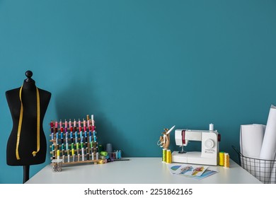 Tailor's workplace with sewing machine, threads and mannequin near blue wall