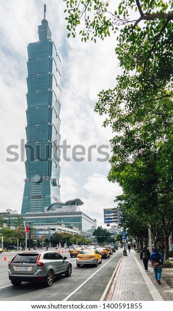 TAIPEI, TAIWAN. DEC 26, 2017:\
Taipei 101 building with tree branches on the right side and cars\
on the road from below with bright blue sky and cloud in Taipei,\
Taiwan.