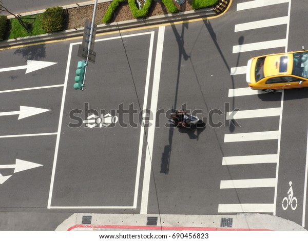 Taipei,Taiwan-August 04,2017:Top view of a motor\
cycle and a taxi in progress move through zebra crossing in the\
noon.Bus,car and motor cycle are important transportation in Taipei\
City.