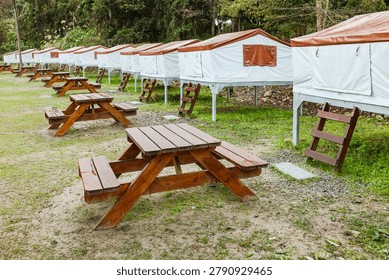 A Taiwan campsite features aligned elevated canvas tents and a central wooden picnic table on grassy ground.