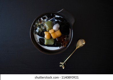 Taiwanese Dessert with Gold Spoon, Singapore dessert, Asian dessert on Black Table with Copy Space. Taiwanese Dessert with Grass Jelly, Taro Balls, Sweet Potato Balls, Fresh Milk, Boba on Wooden Table