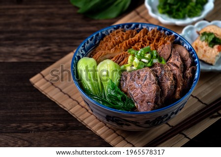 Taiwanese famous food beef noodle soup with sliced braised beef shank, tripe and vegetables on wooden table background.
