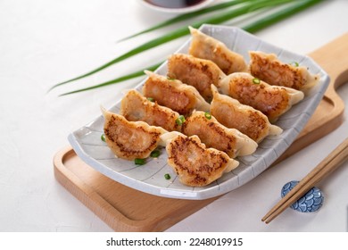 Taiwanese and Japanese Pan-fried gyoza dumpling jiaozi food in a plate with soy sauce on white table background. - Shutterstock ID 2248019915