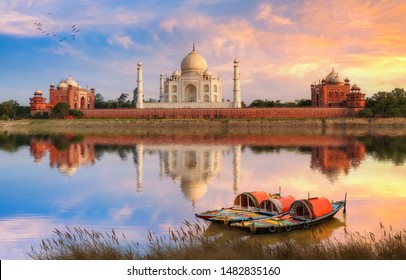 Taj Mahal Agra on the banks of river Yamuna at sunset with moody sky and view of wooden boats used for tourist ride on the river 