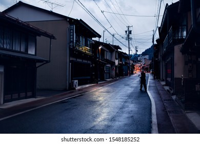 Takayama, Japan - April 8, 2019: Town In Gifu Prefecture In Traditional Village At Night With Illuminated Lantern Lamps And Woman Crossing Street Road