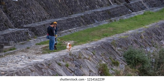 TAKAYAMA, JAPAN - OCTOBER 23RD, 2018. Japanese Couple With Their Pet Dog Walking Along Miyagawa River Banks At Dusk.