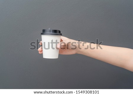 Take away coffee cup background. Female hand holding a coffee paper cup on gray background with clipping path. Close-up image.