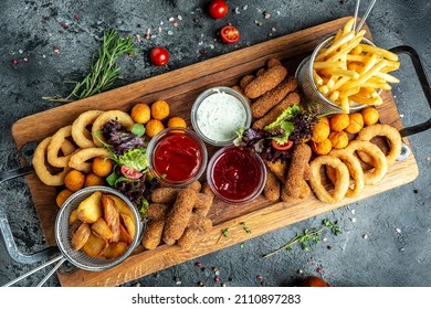 take away food mozzarella sticks, onion rings, french fries, chicken nuggets and sauce on a wooden board. banner, menu, recipe place for text.