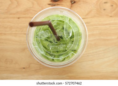 Take away glass of Ice milk green tea with selective focus on the drink and ice inside on wood background from top view shot