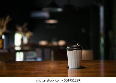 Take Away Hot Coffee Cup On The Wooden Table In The Dark Coffee Cafe Shop Background. 