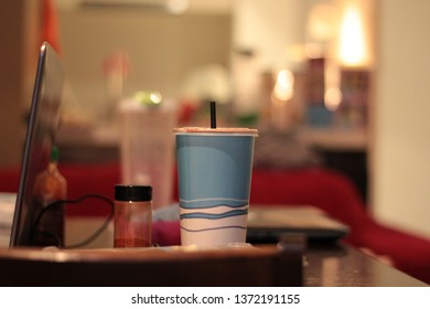 A Take Away Large Soda Cup On A Coffee Table With Some Condiments