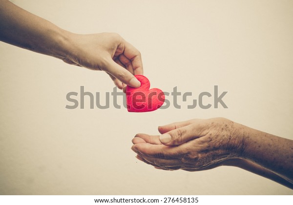 take care of old mother - young female\
hand giving a red heart to old hand of a\
mother