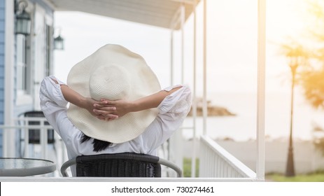 Take It Easy Lifestyle Of Carefree Young Woman Wearing Summer Hat Relaxing Happily Sitting On Porch At Beach-house On Beach Front Enjoying Healthy Living Life Quality For Holiday Vacation Concept