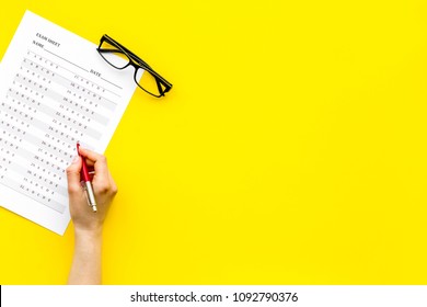 Take the exam, write the exam. Hand with pen near exam paper on yellow background top view copy space