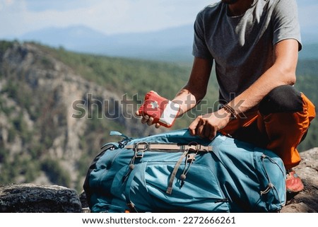 Take a first-aid kit in a backpack on a trip, a hand holds a first aid kit against the background of mountains, equipment in an extreme hike, a white cross