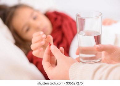 Take It. Close Up Of Red Pill In Hands Of Loving Mother Holding It And Giving It To Her Daughter Lying In Bad