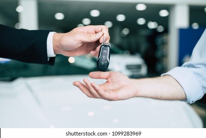 Take the keys. Close up photo of the transfer of keys from the new machine to the buyer against the background of standing cars in the showroom.