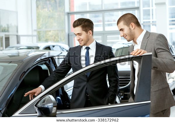 Take a look inside. Car salon\
manager inviting young businessman client to take look inside the\
car