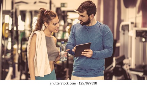 Take A Look At Your Exercise Plan. Young Woman Discussing Workout Progress With Fitness Instructor.