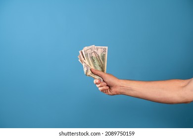 Take my money, the willingness to pay for a cool product, a concept. A man's hand clutches a wad of cash, a photo on a blue background - Shutterstock ID 2089750159